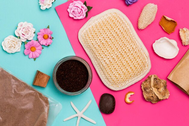 Flat lay of Spa cosmetics products, flowers, scrub, washcloths on colored pink and blue background, top view