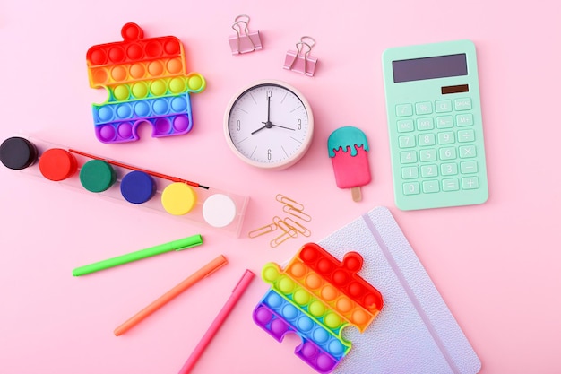 Flat lay of stationery, clock and silicone toys popit on pink background