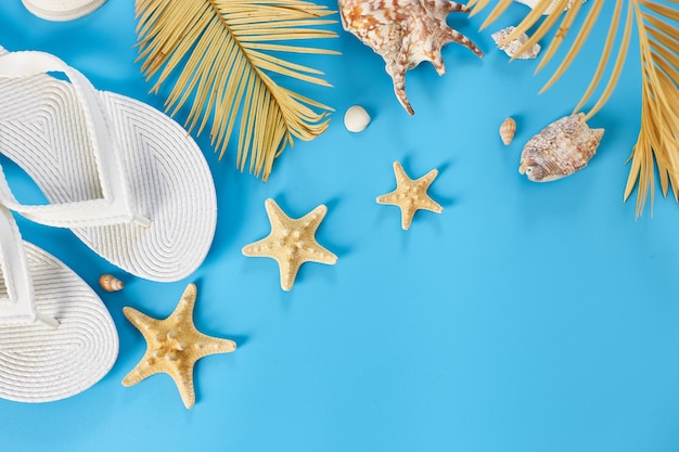 Flat lay summer composition Tropical palm leaves white flip flop seashells on pastel blue background