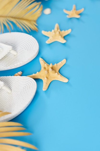 Flat lay summer composition Tropical palm leaves white flip flop seashells on pastel blue background