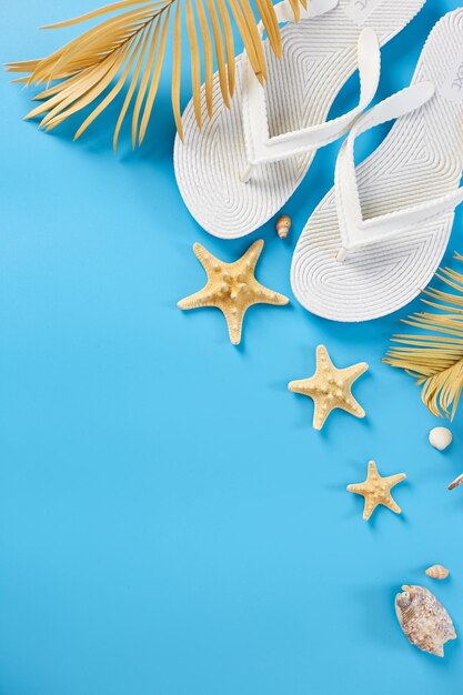 Flat lay summer composition Tropical palm leaves white flip flop seashells on pastel blue background