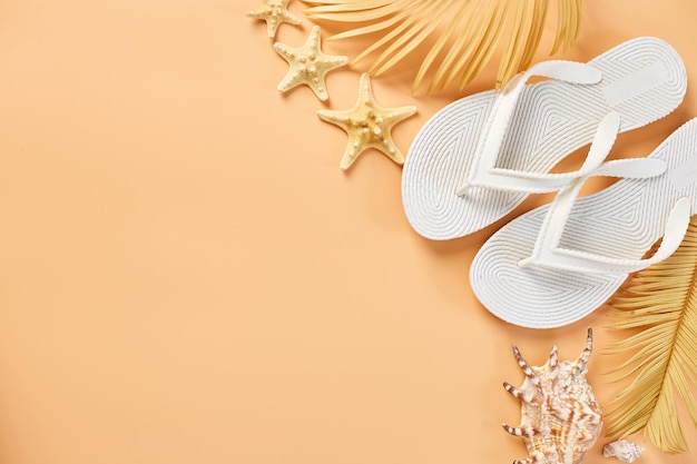 Flat lay summer composition Tropical palm leaves white flip flop seashells on pastel orabge background