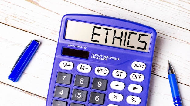 Flat lay or top view of blue pen and calculator with ETHICS text on light wooden table