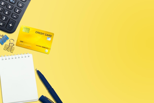 Flat lay or top view of blue pen Notebook Credit card with calculator on vivid yellow background table with blank copy space math cost tax or investment calculation