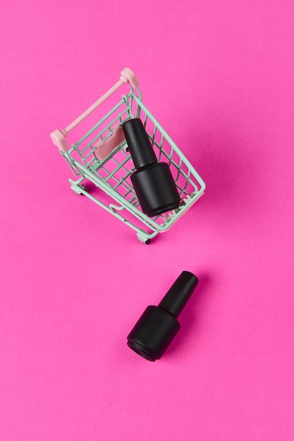 Flat lay top view bottles of nail polish in shopping cart on vibrant pink background