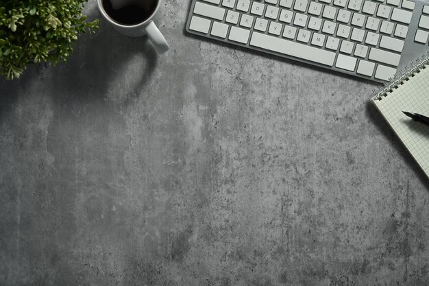 Flat lay top view of keyboard coffee cup and notebook on concrete stone office desk