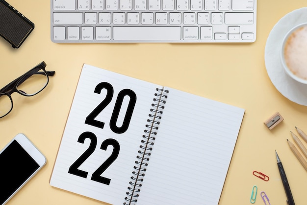 Flat lay top view of office desk working space with laptop smartphone pencil earphones cup of coffee on yellow background You can write messages and new year's resolution in the notebook