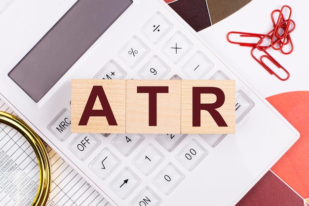 Flat lay top view of office desk Workplace with white calculator magnifying glass red paper clips and wooden cubes with text ATR Average True Range