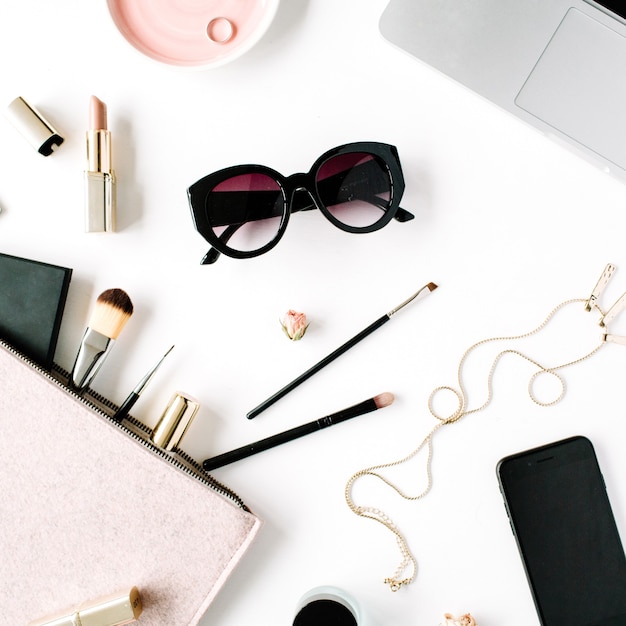 Flat lay, top view office table desk frame. feminine desk workspace with laptop, clutch, cosmetics, phone, sunglasses, lipstick rose buds on white background.