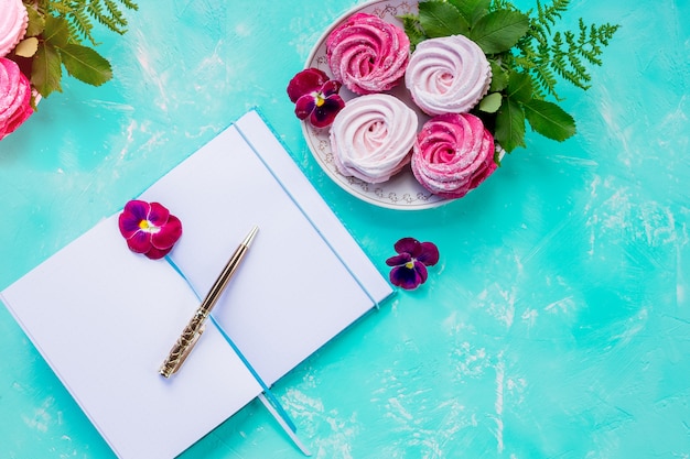 Flat lay top view open blank notebook ,mock up ,on blue wall. Table decorated with wild berry fruit arrangement.pink Meringue..Tasty meringues cookies. Homemade dessert.Copy space