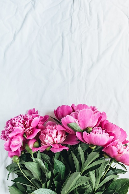 Flat lay, top view of pink peonies flower bouquet on white blanket background