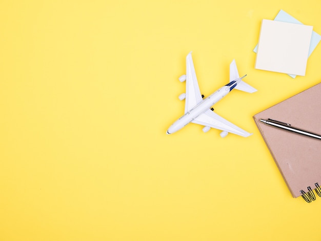 Flat lay top view of a plane on yellow backgrond next to a notebook