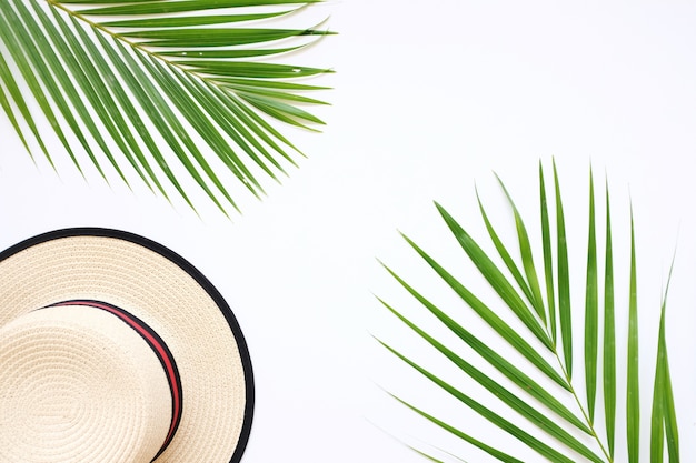 Flat lay of traveler accessories on white background with palm leaf and hat