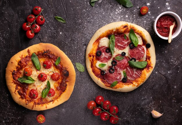 Flat lay of two pizzas with tomatoes and basil on black table