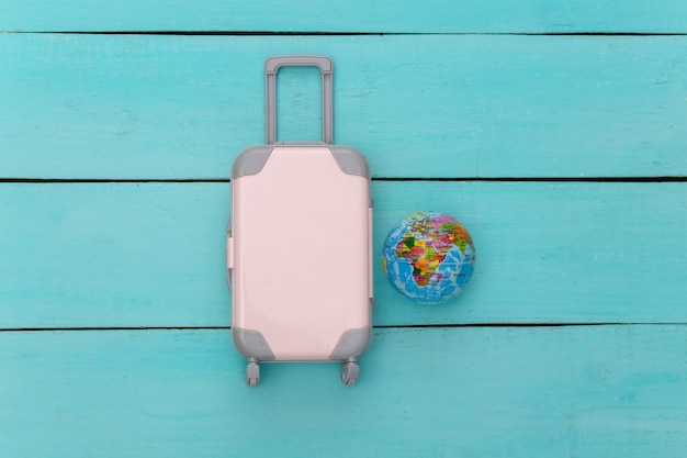 Flat lay vacation holiday and travel planing concept. Mini plastic travel suitcase, globe on blue wooden background. Top view