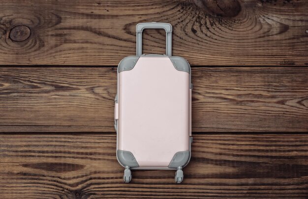 Flat lay vacation holiday and travel planing concept. Mini plastic travel suitcase on wooden background. Top view