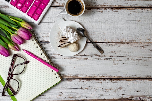 Flat lay view of desktop surface tulips coffee with cake and notepad with calculator on wooden light background holiday in financial sphere