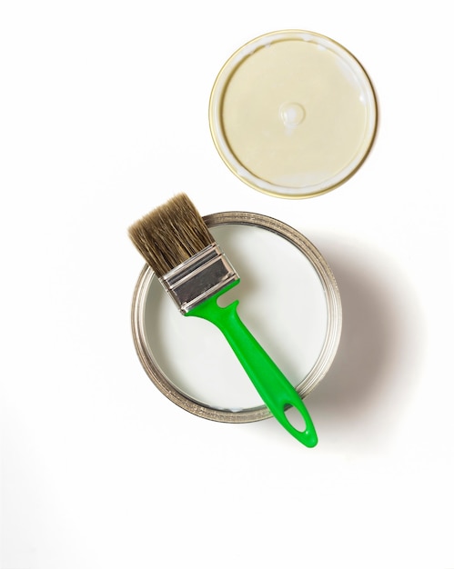 Flat lay on a white background, the view from above, a green brush and an iron can with paint and a lid.