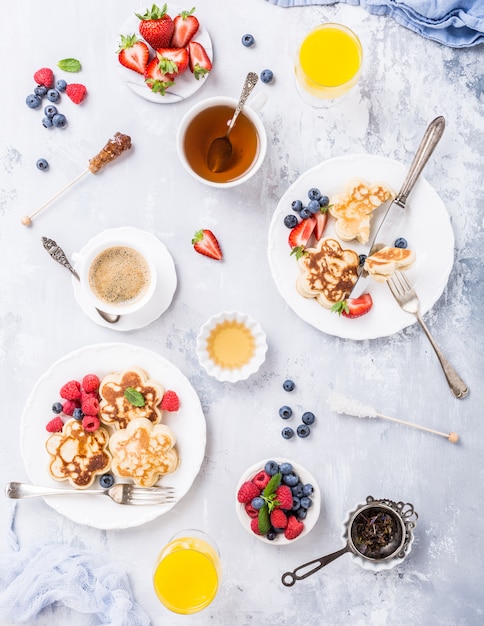 Flat lay with breakfast with scotch pancakes in flower form, berries and honey on light wooden table. 