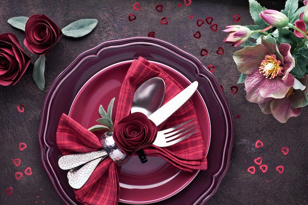 Flat lay with burgindy plates and crockery decorated with roses and anemones, Christmas or Valentine dinner setup