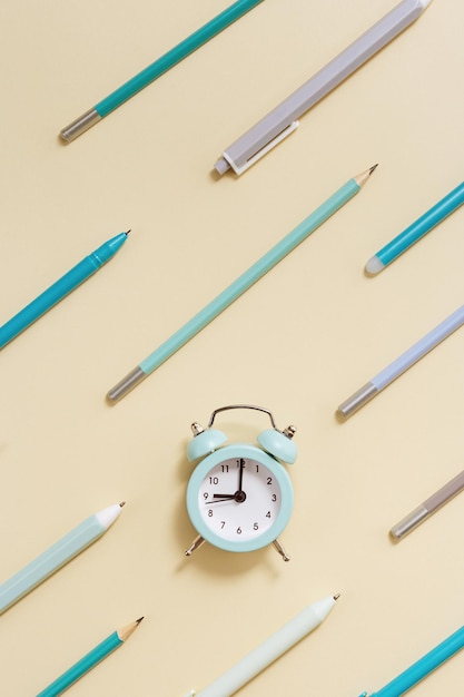 Flat lay with clock and geometric pattern from blue pens and pencils on beige Time to go to school