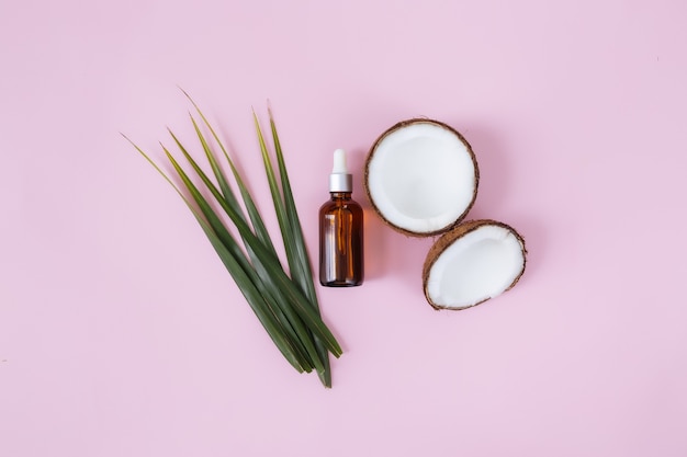 Flat lay with cut halves of coconut and green palm leaf, glass bottle with essential oil. Exotic fruit.