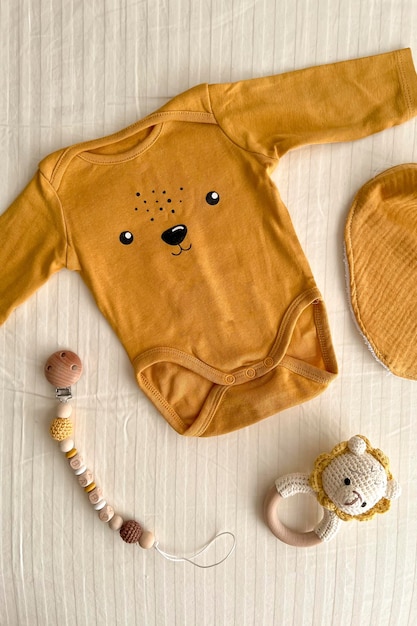 A flat lay with cute newborn baby clothes and ecofriendly accessories on a light sheet in the crib Online fashion store online shopping branding concept Bodysuit rattle nipple clothespin bib