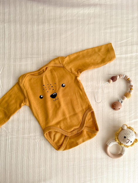 A flat lay with cute newborn baby clothes and ecofriendly accessories on a light sheet in the crib Online fashion store online shopping branding concept Bodysuit rattle and nipple clothespin