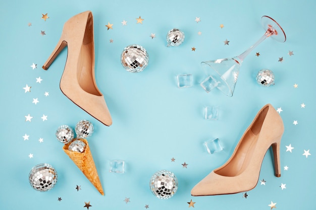 Flat lay with female shoes, disco balls, ice cubes, cocktail glass and confetti.