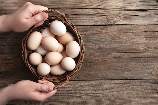 Flat lay with hands holding basket with organic chicken eggs on wooden background. Organic household concept with eggs from free-range and pasture raised hens