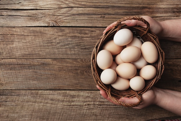 Flat lay with hands holding basket with organic chicken eggs on wooden background. Organic household concept with eggs from free-range and pasture raised hens