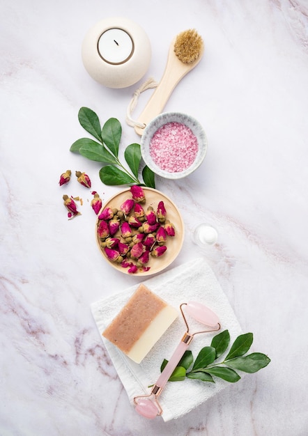 Flat lay with organic sea salt with dried rose flowers soap candle brush and gua sha on a pink marble background The concept of a natural spa product Top view Vertical orientation