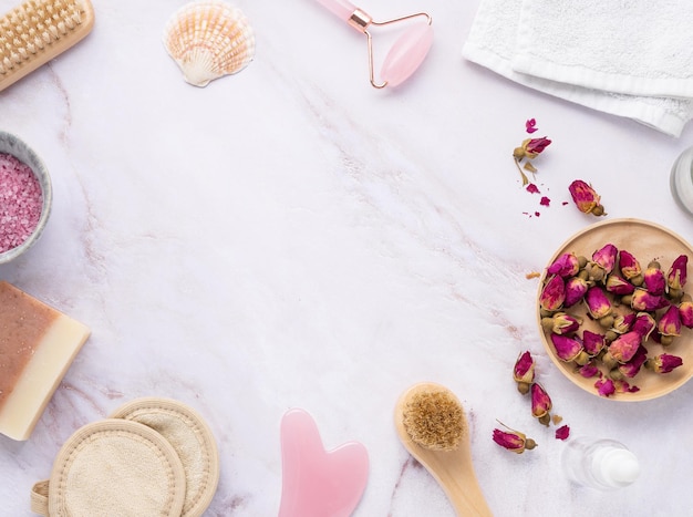 Flat lay with organic sea salt with dried rose flowers soap candle brush and gua sha on a pink marble background in frame The concept of a natural spa product Top view and copy space