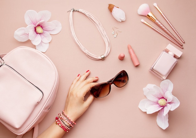 Flat lay with pink woman accessories  with backpack and woman hand holding the sunglasses. Summer fashion trends, shopping idea