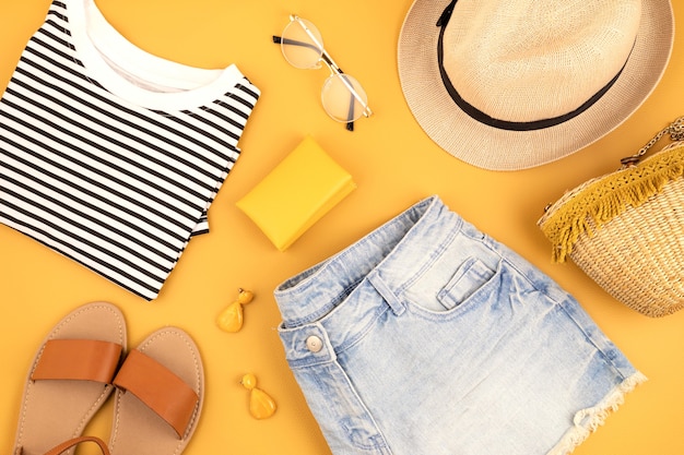 Flat lay with woman fashion accessories, jeans shorts, hat, sunglasses over yellow wall. Fashion, online beauty blog, summer style, shopping and trends concept. Top view