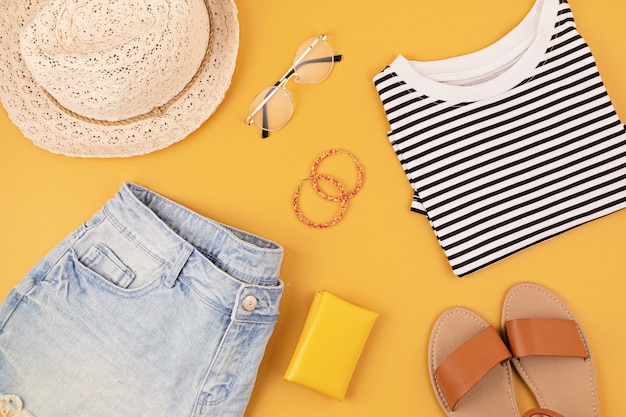 Flat lay with woman fashion accessories, jeans shorts, hat, sunglasses over yellow wall. Fashion, online beauty blog, summer style, shopping and trends concept. Top view