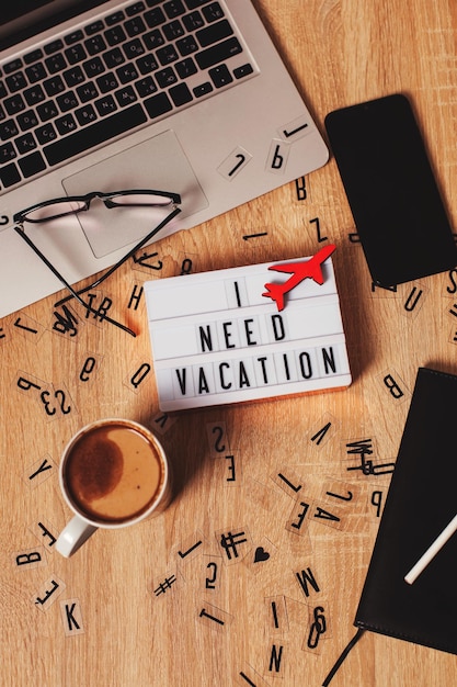 Photo flat lay on a wooden table a light box with the inscription i need a vacation a plane symbol a lapto...