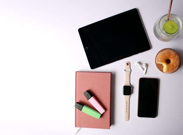 flat lay of working space with tablet, notebook, phone, smartwatch, headsets, coffee, donut