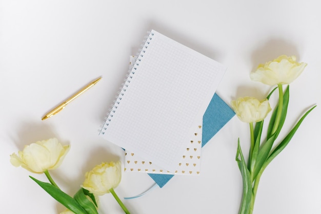 Flat lay workspace of a blogger or freelancer with yellow spring tulips stationery on a white background with a blank sheet of notepad paper