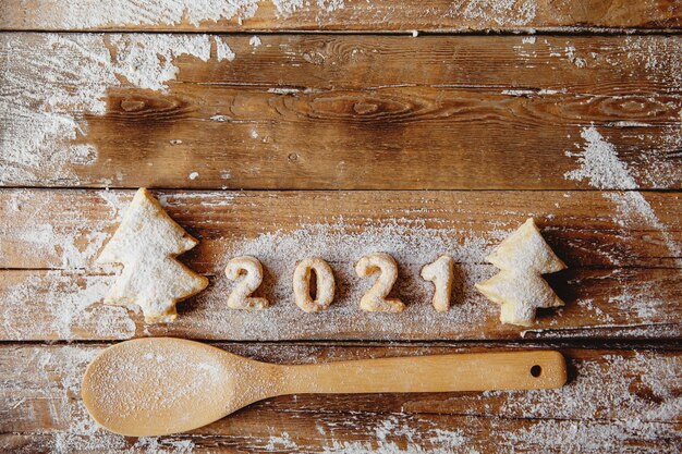 Flat layout on a wooden table with a wooden spoon and cookies in the shape of Christmas trees