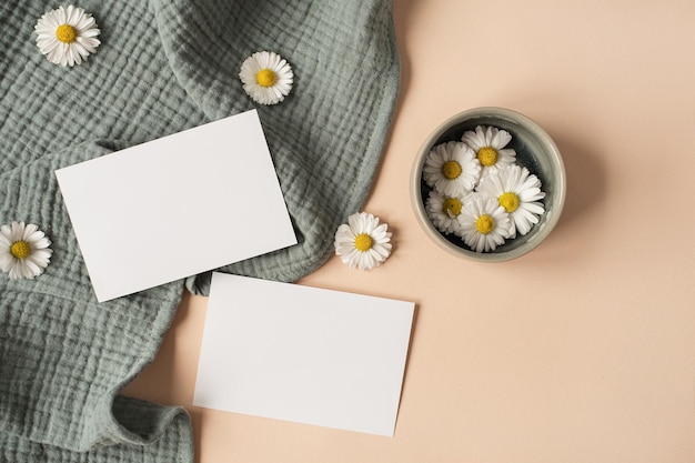 Flatlay aesthetic Parisian styled invitation template Blank paper sheet card with mockup copy space chamomile flower buds and aquamarine muslin cloth on neutral beige background Flat lay top view