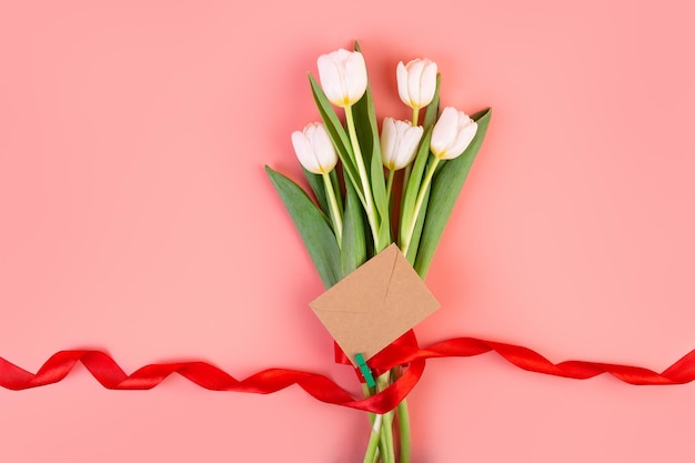 flatlay A beautiful bouquet tied with a red ribbon and an envelope isolated pastel pink background