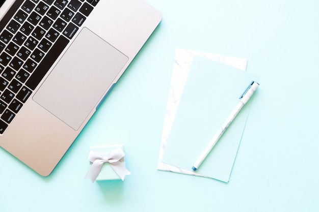 Flatlay of laptop, paper, pen and little gift box on a blue 