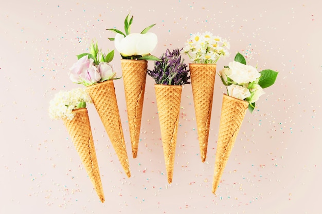 Photo flatlay of waffle cones with flowers over pastel light pink background top view