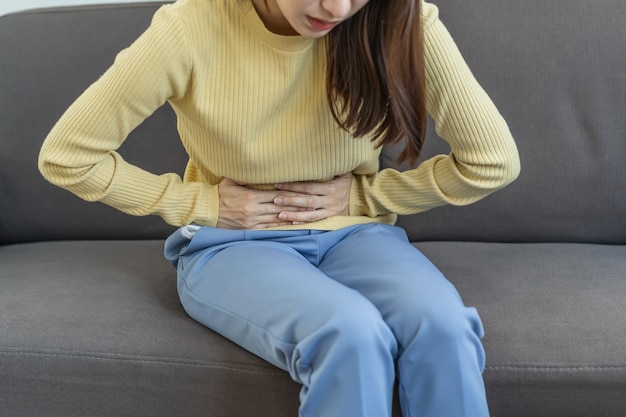 Photo flatulence asian young woman, girl hand in stomach ache, suffer from food poisoning, abdominal pain and colon problem, gastritis or diarrhoea. patient belly, abdomen or inflammation, concept.