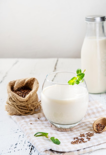 Flax seed homemade milk in glass and bottle on white wooden background with napkin and seeds aside