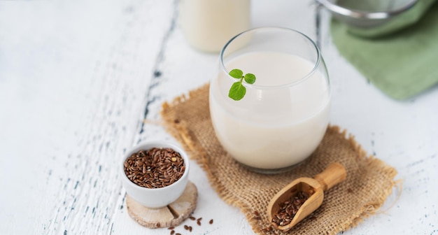 Flax seed milk in glass and bottle mint leaf seeds aside white wooden background