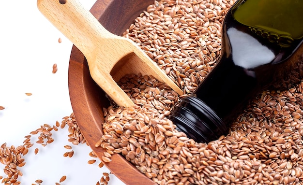 Flax seeds or linseeds in spoon and bowl with glass of linseed oil on wooden plate on white background Flaxseed or linseed concept Copy space