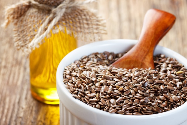 Flax seeds and oil in bottle on wooden background