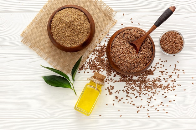 Flaxseeds in a spoon and bowl with a bottle of flaxseed oil and flaxseed flour